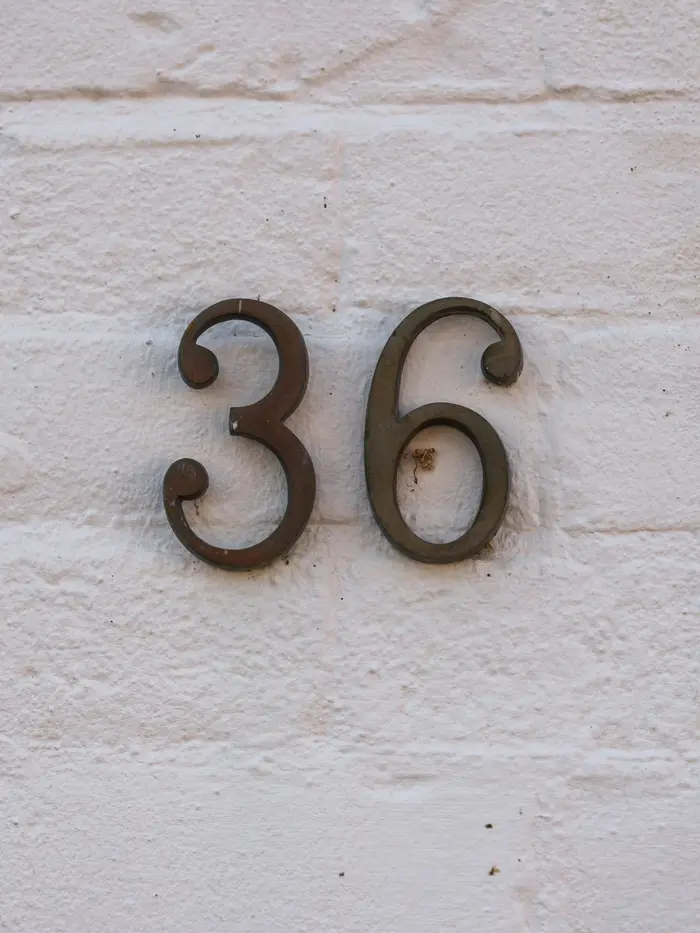 Número de casa en metal sobre un muro blanco.